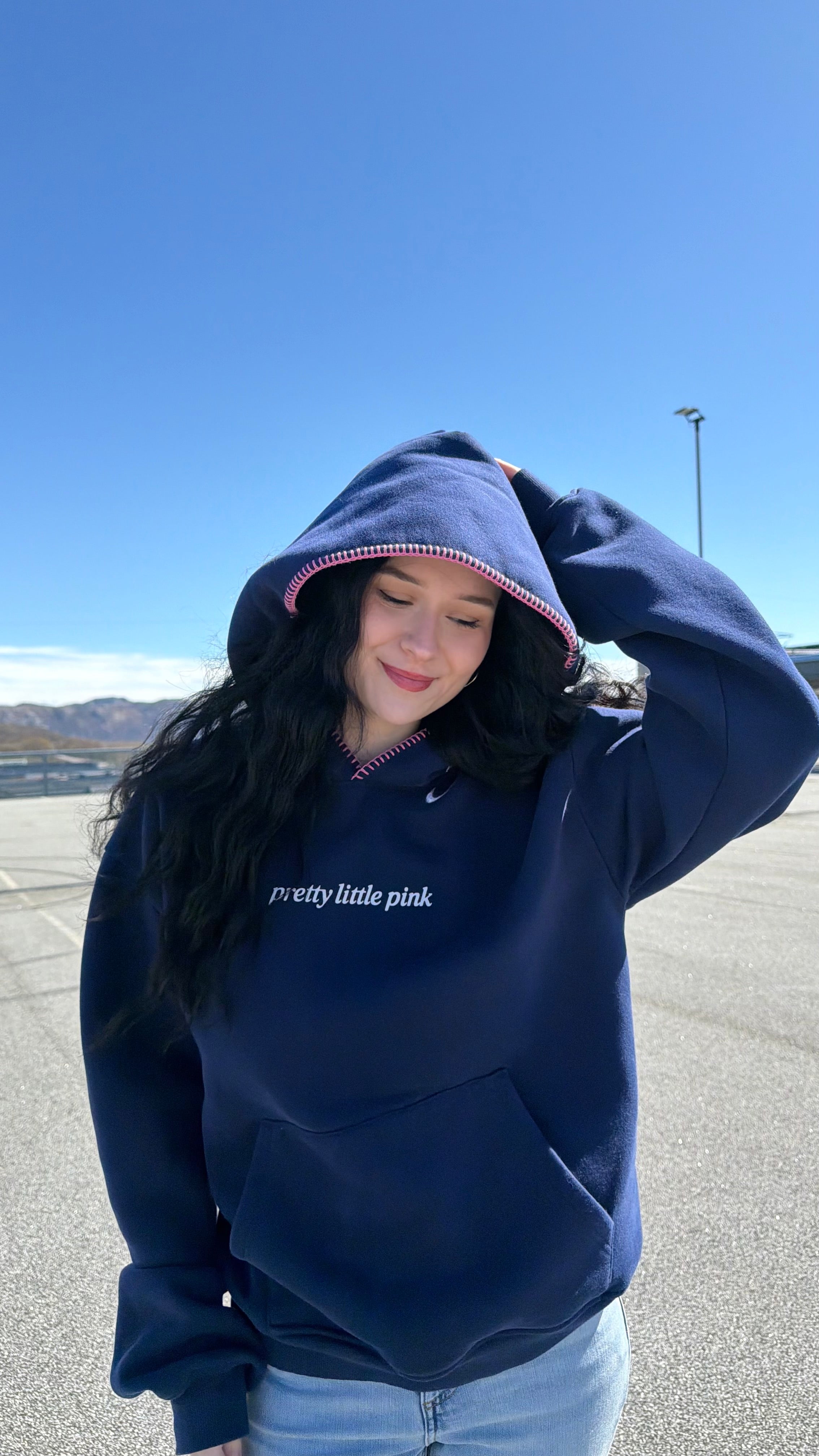 Person wearing a navy hoodie with text, standing outdoors on a clear day.